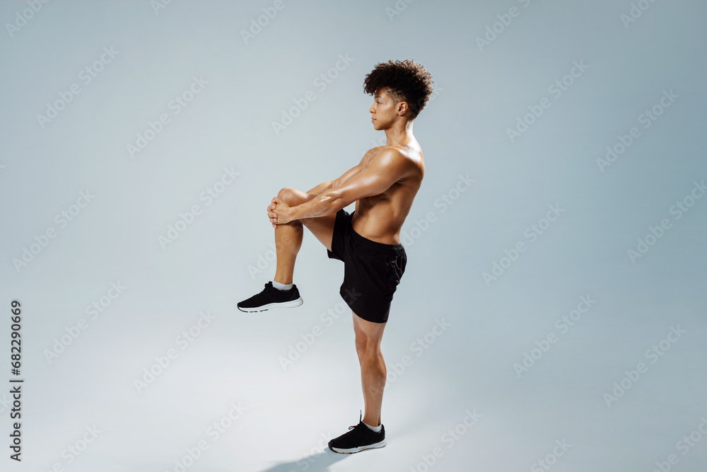 sportsman standing doing knee to chest stretch exercise, gray background sportsman standing doing knee to chest stretch exercise, gray background