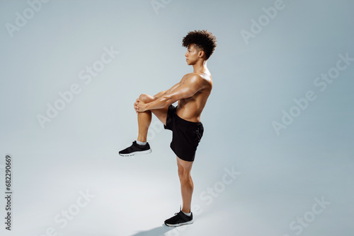 sportsman standing doing knee to chest stretch exercise, gray background photo