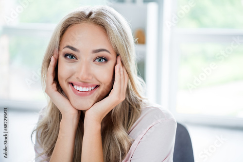 Photo portrait of cheerful adorable girl two arms touch cheeks enjoy good mood cozy home modern house room indoors