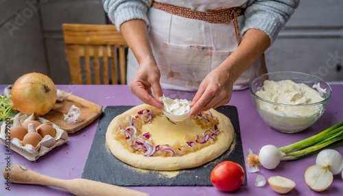 close up woman cover dough for an alsatian tarte cake on a purple kitchen surface next to it are the ingredients for the tarte flambee traditional tarte flambee with creme fraiche onion and bacon