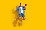 Full size photo of ecstatic guy wear jeans jacket jumping look empty space scream in loudspeaker isolated on yellow color background