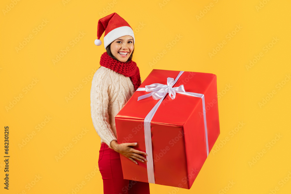 woman in Santa hat cheerfully holding large Christmas present, studio woman in Santa hat cheerfully holding large Christmas present, studio