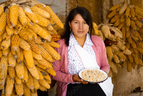 Mujer andina latinoamericana sosteniendo un plato al fondo maíz colgados en la casa producción, Cultura, estilo de vida saludable,