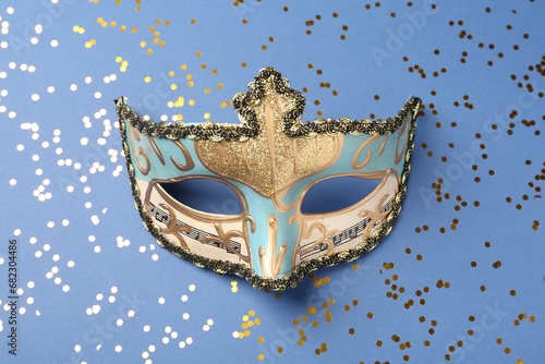 Beautiful carnival mask and shiny confetti on blue background, top view