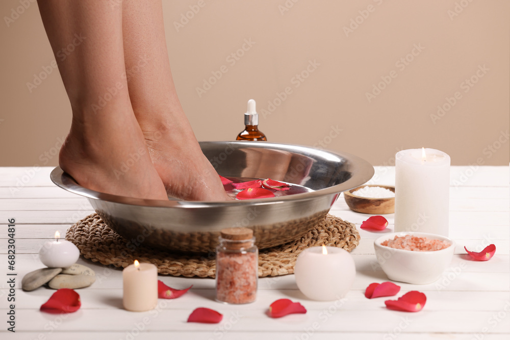 Woman soaking her feet in bowl with water and rose petals on white wooden surface, closeup. Pedicure procedure Woman soaking her feet in bowl with water and rose petals on white wooden surface, closeup. Pedicure procedure