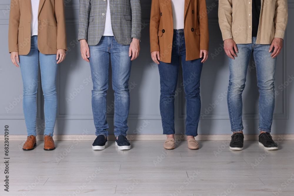 Group of people in stylish jeans near light grey wall indoors, closeup