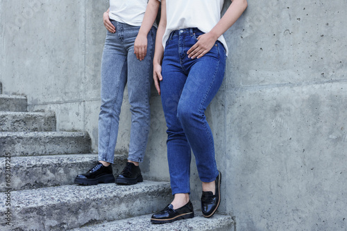 Women in stylish jeans on stairs near stone wall outdoors, closeup