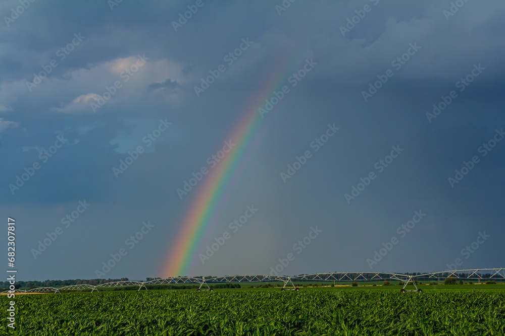 Large irrigation system in a green field, with a beautiful rainbow forming in the spray against a backdrop of cloudy skies Large irrigation system in a green field, with a beautiful rainbow forming in the spray against a backdrop of cloudy skies