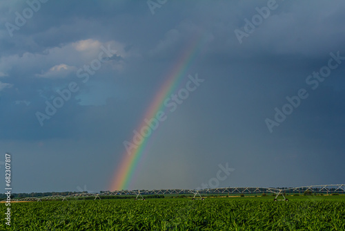 Large irrigation system in a green field, with a beautiful rainbow forming in the spray against a backdrop of cloudy skies
