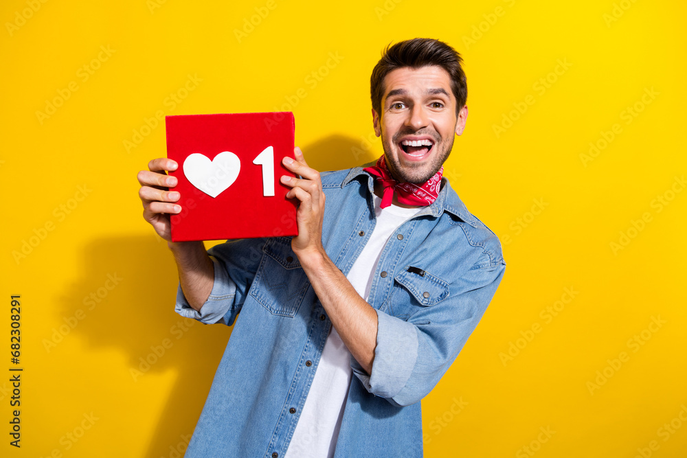 Photo portrait of attractive young man hold excited heart notification wear trendy jeans clothes isolated on yellow color background Photo portrait of attractive young man hold excited heart notification wear trendy jeans clothes isolated on yellow color background