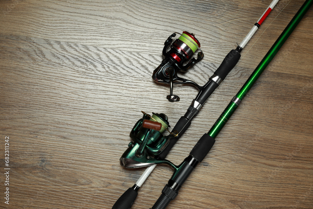 Fishing rods with spinning reels on wooden background, top view. Space for text