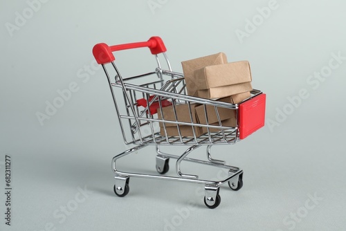 Small metal shopping cart with cardboard boxes on light background