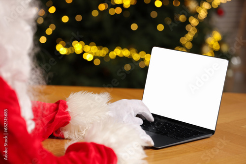 Merry Christmas. Santa Claus using laptop at table against blurred lights  closeup