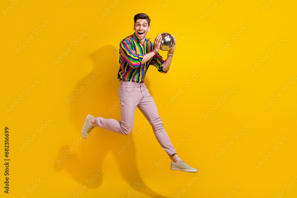 Full body photo of ready to party man catching small disco ball during performance concert he jumping isolated on yellow color background Full body photo of ready to party man catching small disco ball during performance concert he jumping isolated on yellow color background