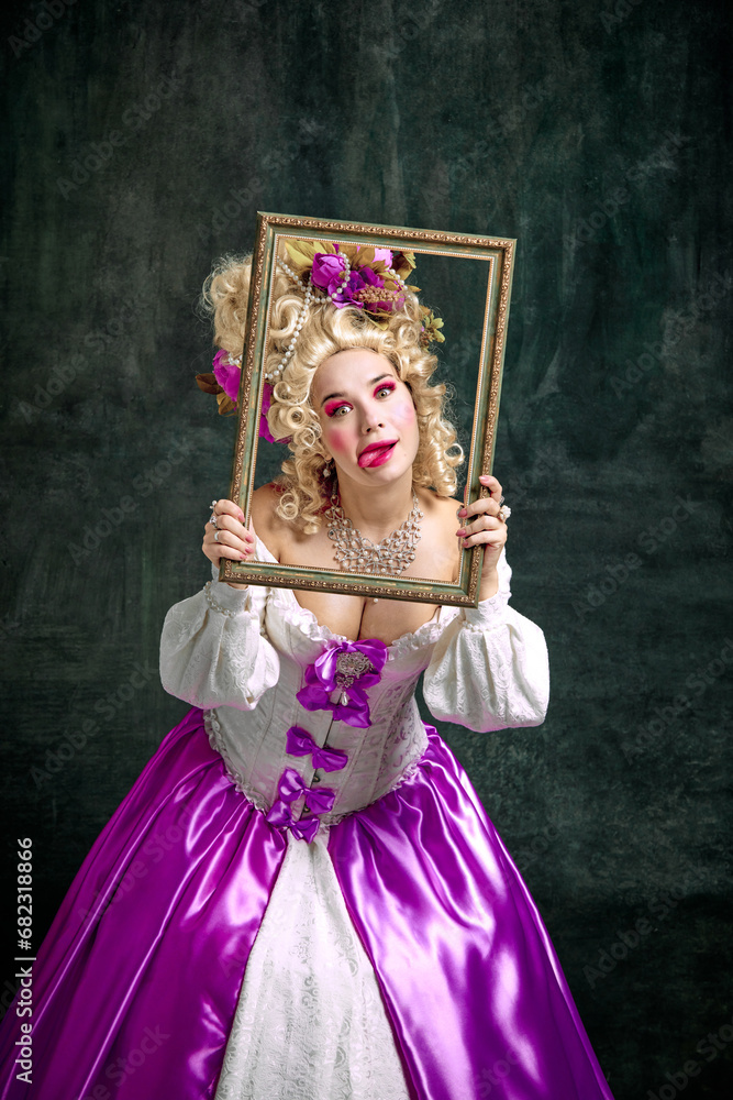 Woman dressed like classic historical character, in old-fashioned dress holding retro frame and grimacing looking at camera over vintage background.