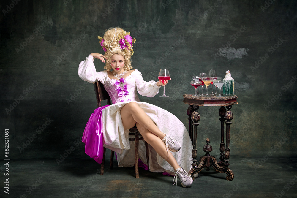 Serious princess, aristocratic medieval person in old-fashioned dress and modern shoes sitting holding cocktail against vintage background. - obrazy, fototapety, plakaty 