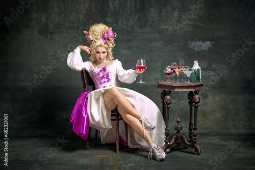 Serious princess, aristocratic medieval person in old-fashioned dress and modern shoes sitting holding cocktail against vintage background.