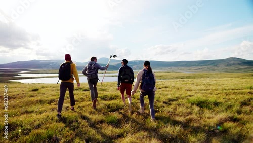 Group of four young hikers walk trail to wild river at scenic mountain landscape rear view. Trekking path, travel freedom and motivating tourist recreation