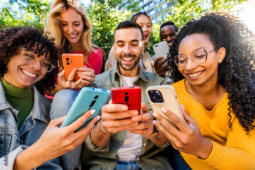 Group of young people using smart mobile phone outdoors - Happy friends with smartphone laughing together watching funny video on social media platform - Tech and modern life style concept photo