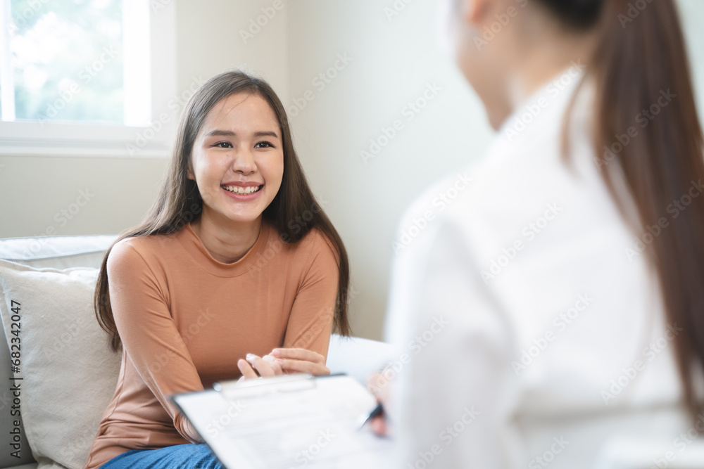 Happy young Asian woman talking with the psychologist during depressed mental health therapy at the clinic. - obrazy, fototapety, plakaty 