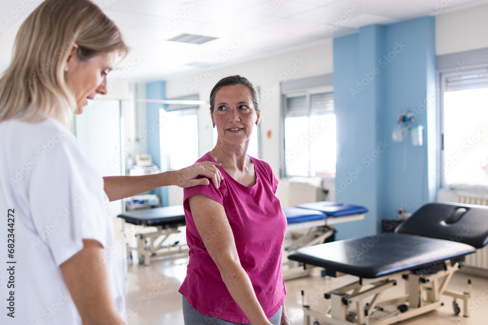 Obraz premium The middle aged female patient is in the rehabilitation gym while her physical therapist teaches her how to do some exercises.