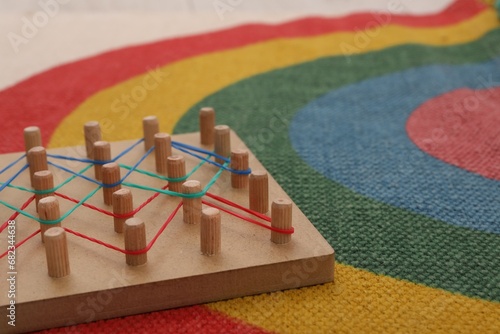 Wooden geoboard with rubber bands on carpet, closeup. Space for text. Educational toy for motor skills development photo