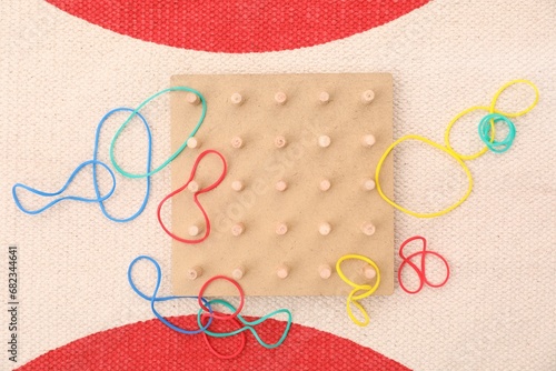 Wooden geoboard and rubber bands on carpet, flat lay. Educational toy for motor skills development photo