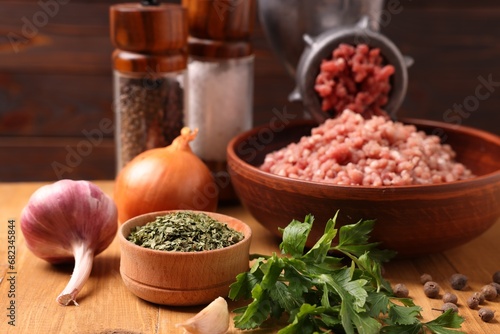 Manual meat grinder with beef mince, spices and parsley on wooden table, selective focus photo