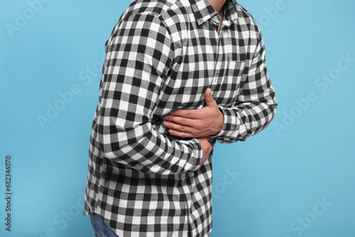 Man suffering from stomach pain on light blue background, closeup