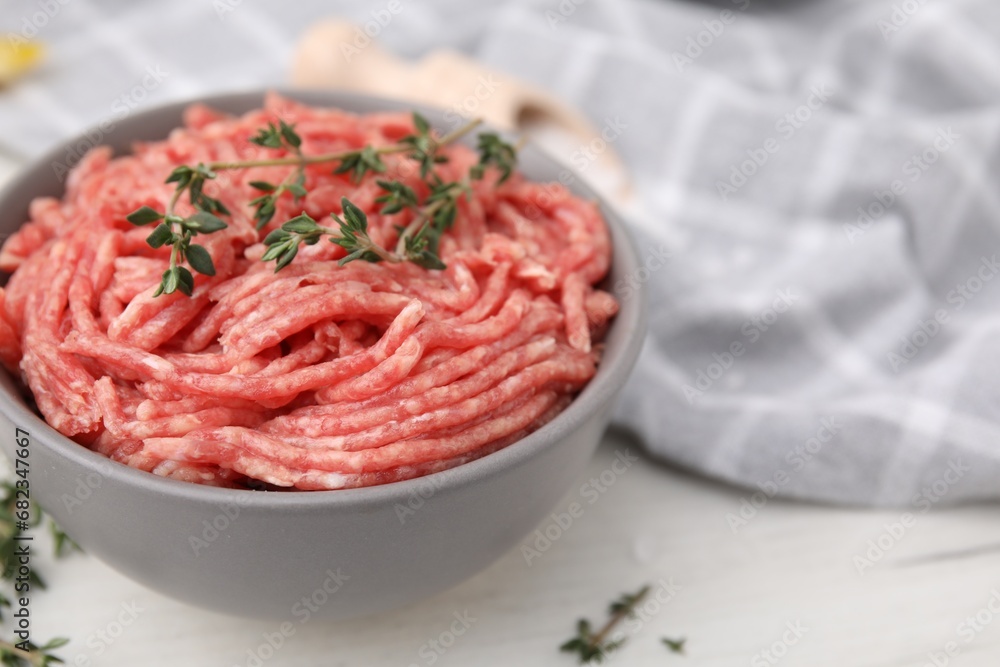 Fresh raw ground meat and thyme in bowl on white table, closeup. Space for text Fresh raw ground meat and thyme in bowl on white table, closeup. Space for text