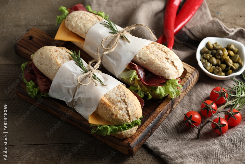 Delicious sandwiches with bresaola, lettuce and other products on wooden table