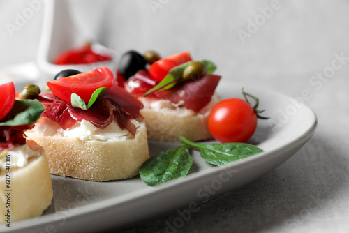 Delicious sandwiches with bresaola, cream cheese, olives and tomato on light grey table, closeup