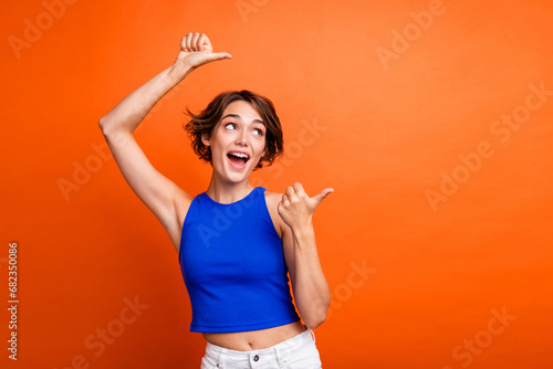 Photo of impressed excited girl dressed blue top looking pointing two thumbs empty space isolated orange color background