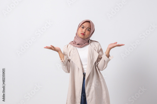Portrait of confused Asian hijab woman in casual suit spreading hands sideways, feeling doubt while making choice. Businesswoman concept. Isolated image on white background