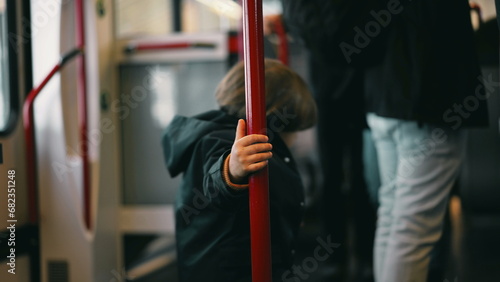 whimsical Little traveler on a train, clutching a metal support bar and twirling around it. A snapshot of childhood joy, making the best of the commute with innocent play