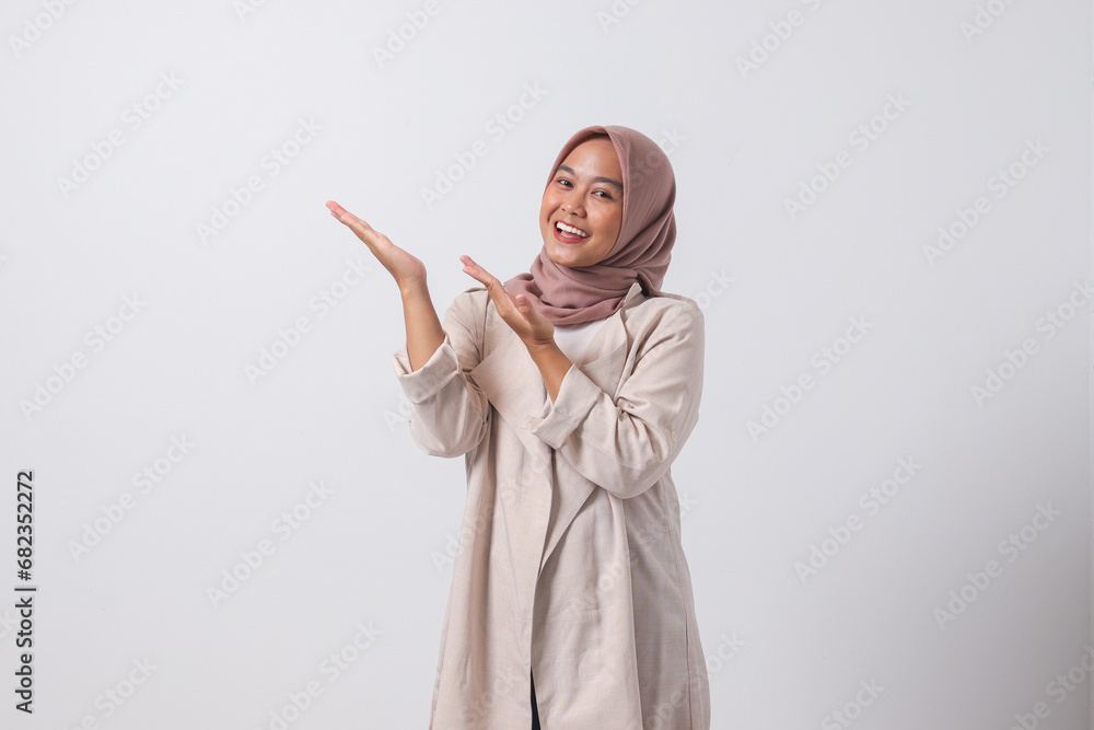 Portrait of excited Asian hijab woman in casual suit pointing and showing product in her side with finger. Businesswoman concept. Isolated image on white background Portrait of excited Asian hijab woman in casual suit pointing and showing product in her side with finger. Businesswoman concept. Isolated image on white background