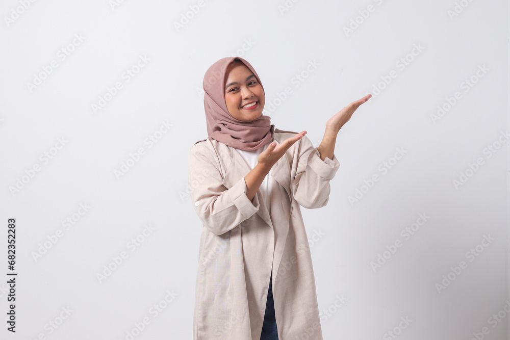 Portrait of excited Asian hijab woman in casual suit pointing and showing product in her side with finger. Businesswoman concept. Isolated image on white background Portrait of excited Asian hijab woman in casual suit pointing and showing product in her side with finger. Businesswoman concept. Isolated image on white background