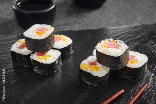  Delicate maki sushi rolls filled with fresh tuna and sweet mango, artfully displayed on a black slate with soy sauce on the side