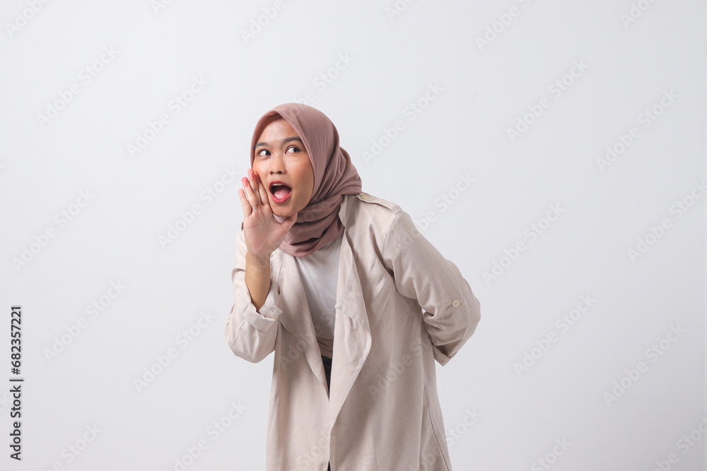 Portrait of excited Asian hijab woman in casual suit screaming announcement and whispering gossip. Businesswoman concept. Isolated image on white background Portrait of excited Asian hijab woman in casual suit screaming announcement and whispering gossip. Businesswoman concept. Isolated image on white background
