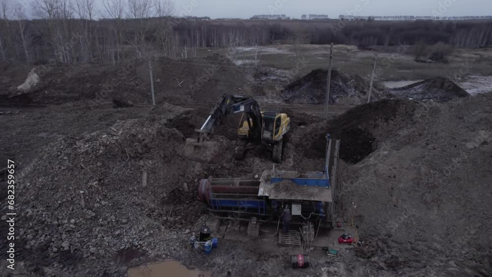 Excavator works on construction site. Workers use excavator on building site in mining industry. Excavator waits for sifting machine to break up soil Excavator works on construction site. Workers use excavator on building site in mining industry. Excavator waits for sifting machine to break up soil