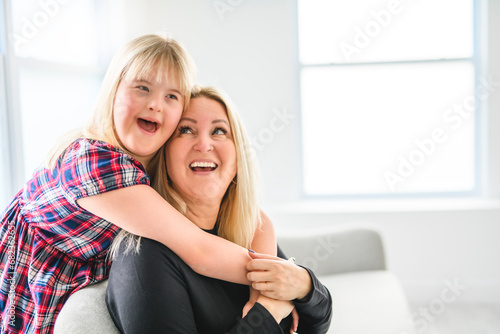 Mother and sweet down syndrome daughter girl at home sofa photo