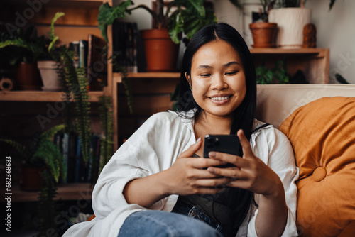 Cheerful asian woman using smartphone while sitting at home