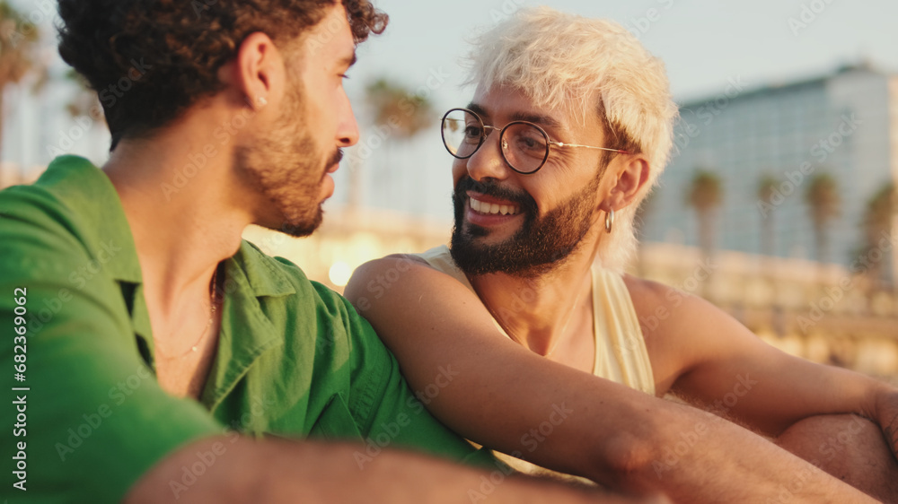Close up, beautiful gay couple in love talking and laughing while sitting on the beach at dawn Close up, beautiful gay couple in love talking and laughing while sitting on the beach at dawn