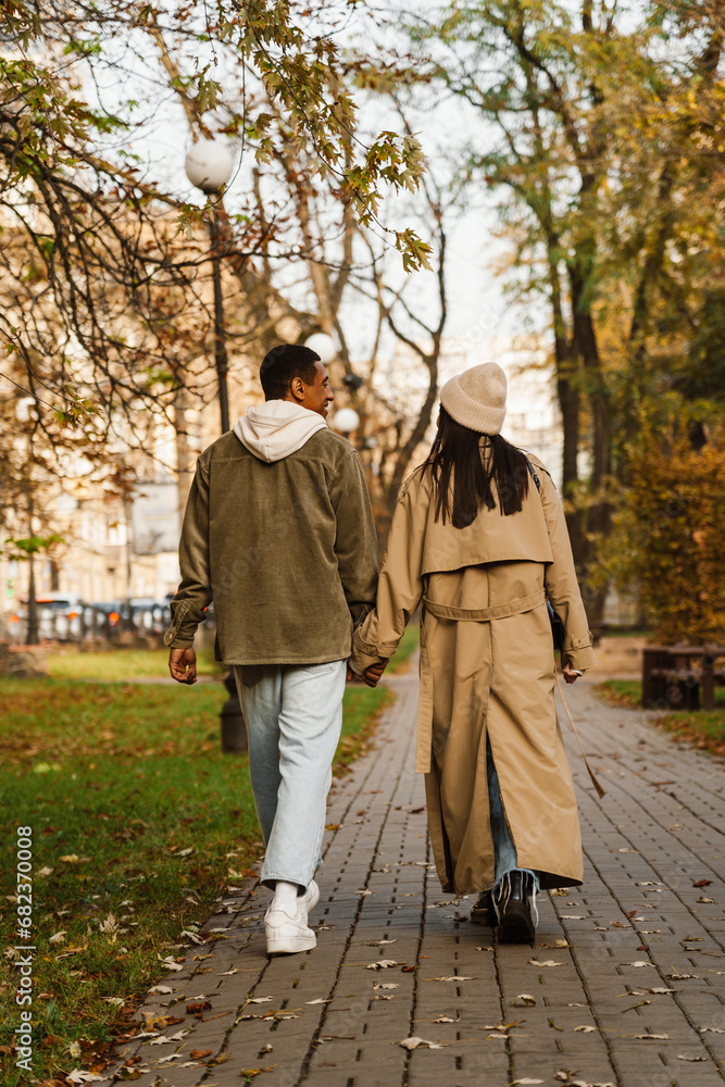 Back view of young couple holding hands while walking in park