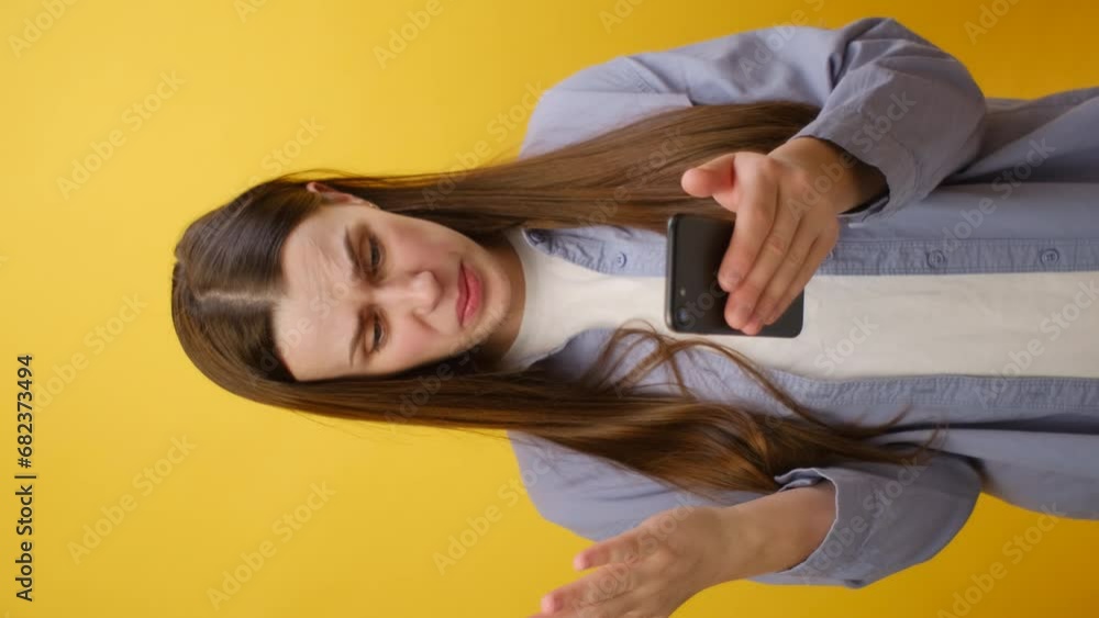 Vertical shot of irritated young caucasian woman wearing shirt using mobile cell phone swear read fake news unexpected rumor has some problems, isolated on yellow background. People lifestyle concept Vertical shot of irritated young caucasian woman wearing shirt using mobile cell phone swear read fake news unexpected rumor has some problems, isolated on yellow background. People lifestyle concept