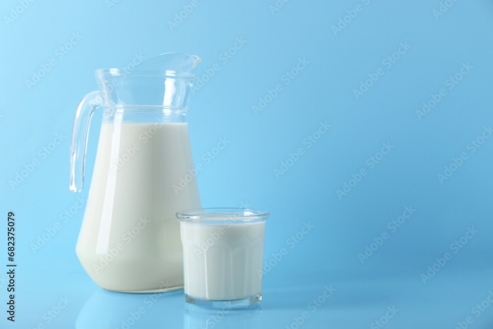 Jug and glass of fresh milk on light blue background, space for text Jug and glass of fresh milk on light blue background, space for text