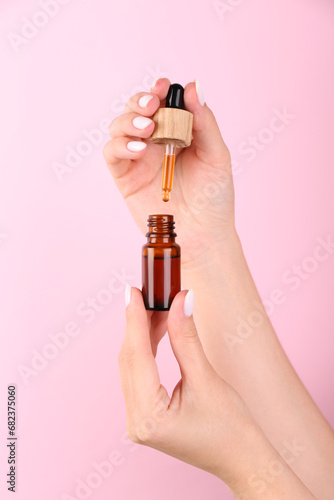 Woman holding bottle of essential oil on pink background, closeup