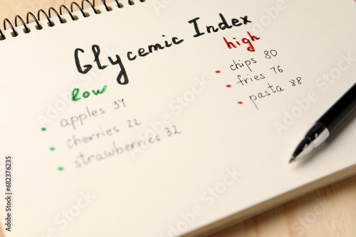 List with products of low and high glycemic index in notebook and pen on table, closeup