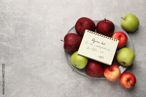 Fototapeta Naklejka Na Ścianę i Meble -  Notebook with calculated glycemic load for apples and fresh fruits on light grey textured table, top view. Space for text