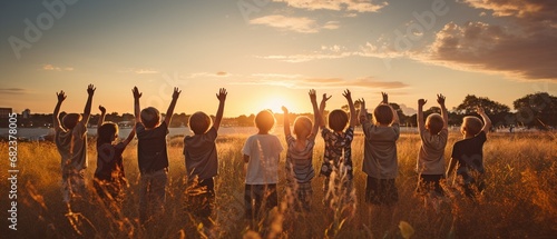 Friendship group of children raising their hands in a queue at dusk on the verdant park grass. . photo